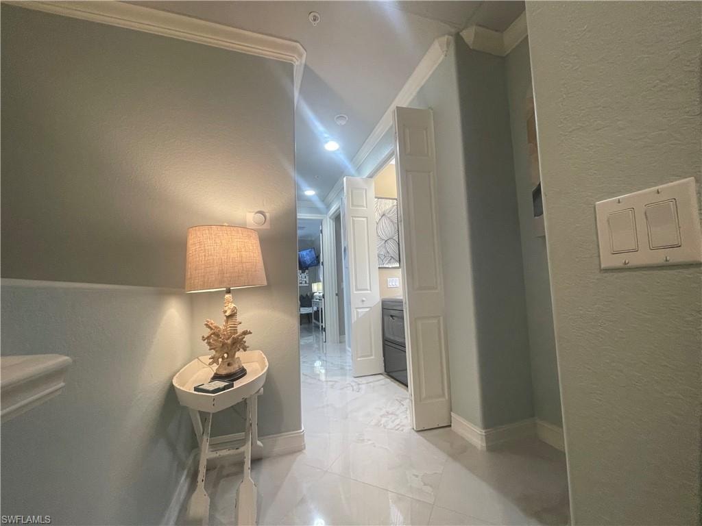 Hall featuring a textured wall, ornamental molding, and light marble finish floors