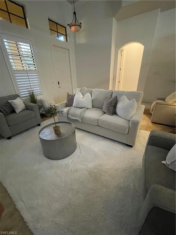 Living area with a towering ceiling, arched walkways, and carpet floors
