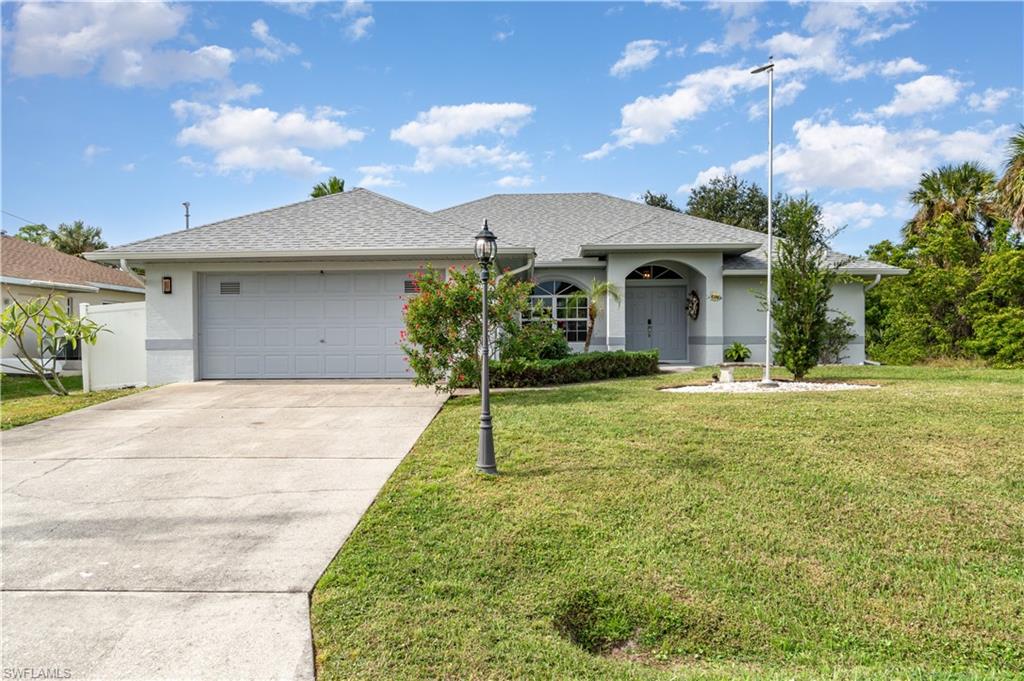 Ranch-style home with a shingled roof, a front lawn, an attached garage, driveway, and stucco siding