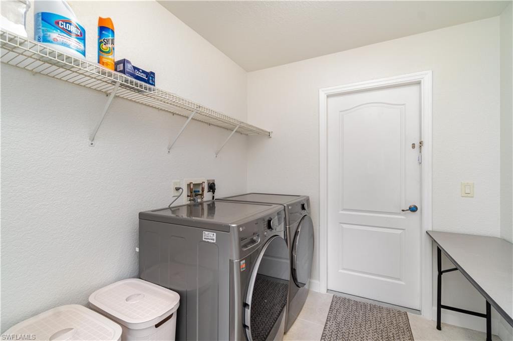 Laundry area featuring washing machine and clothes dryer, light tile patterned flooring, and a textured wall