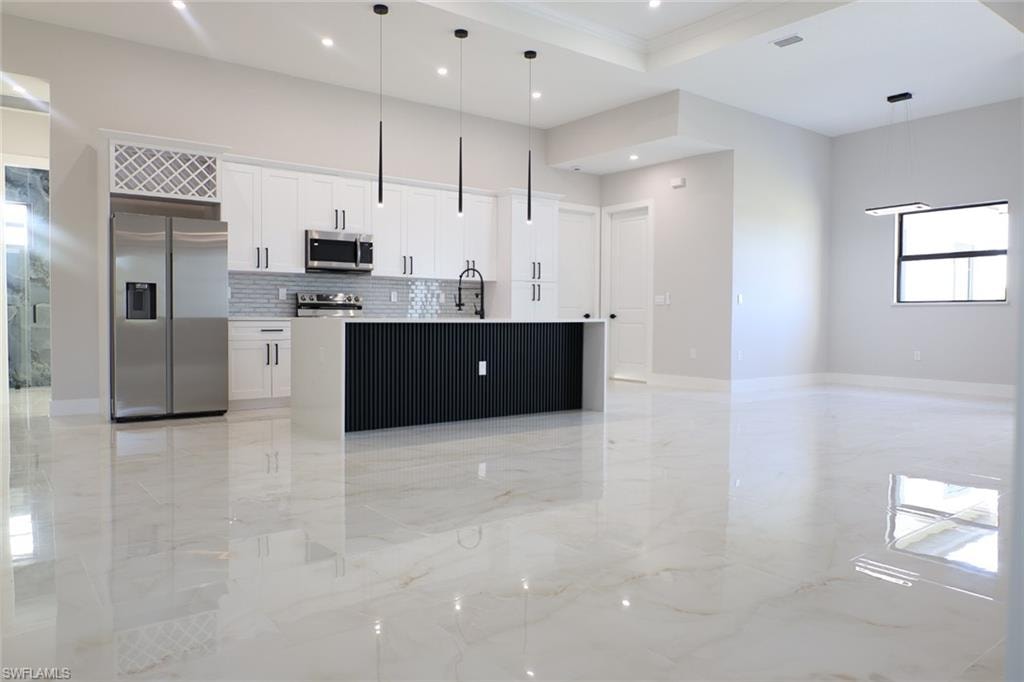 Kitchen featuring open floor plan, a kitchen island with sink, stainless steel appliances, white cabinets, and light marble finish flooring