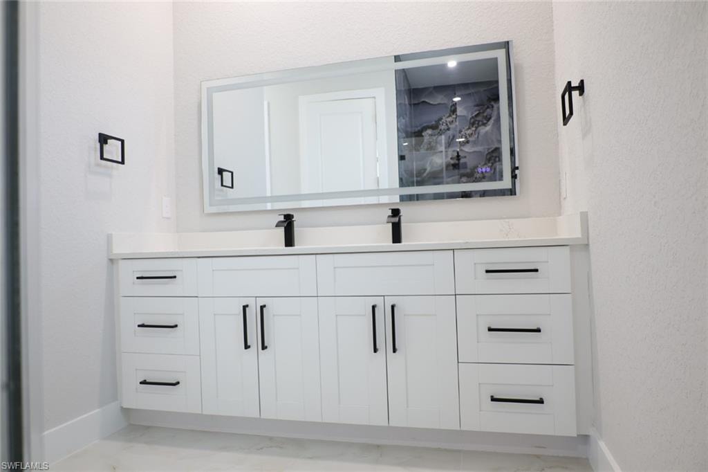 Bathroom with double vanity, a textured wall, and light marble finish flooring
