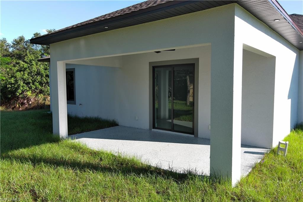 Rear view of property featuring stucco siding, a patio area, and a lawn