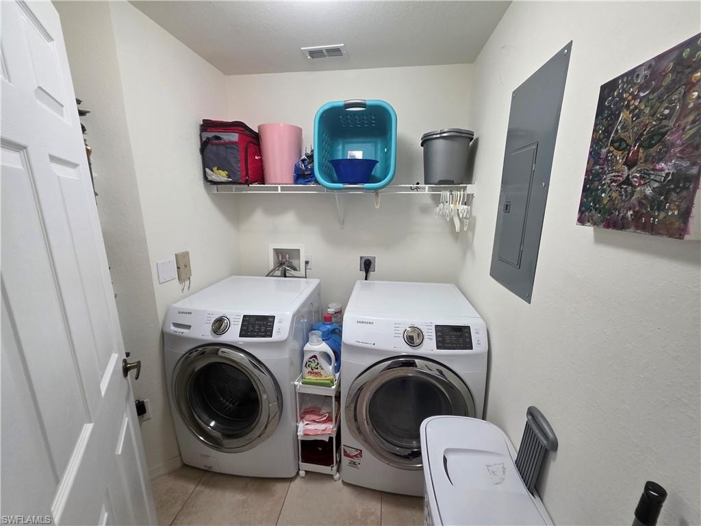 Washroom with light tile patterned floors, washer and clothes dryer, and electric panel