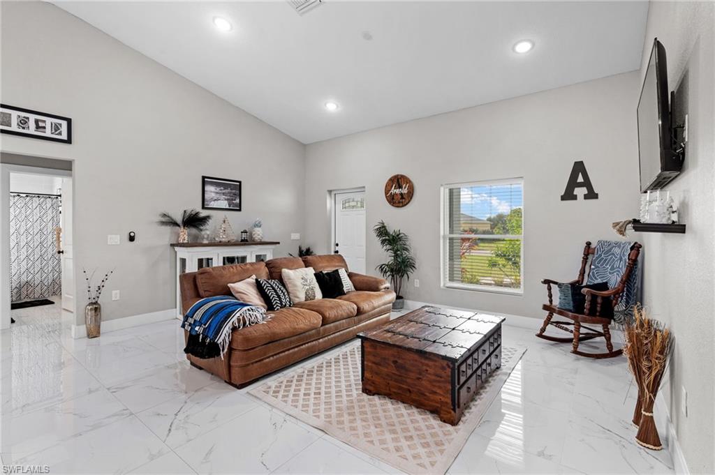 Living room featuring vaulted ceiling, light marble finish flooring, and recessed lighting