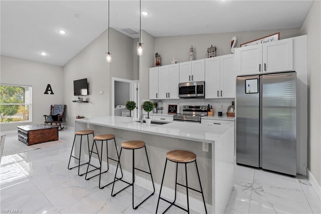 Kitchen with stainless steel appliances, light stone countertops, decorative light fixtures, white cabinetry, and a breakfast bar area
