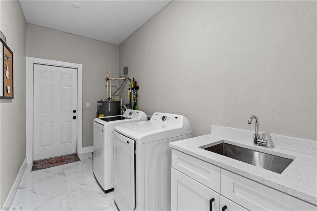 Laundry area featuring light marble finish flooring, washing machine and dryer, electric water heater, and cabinet space