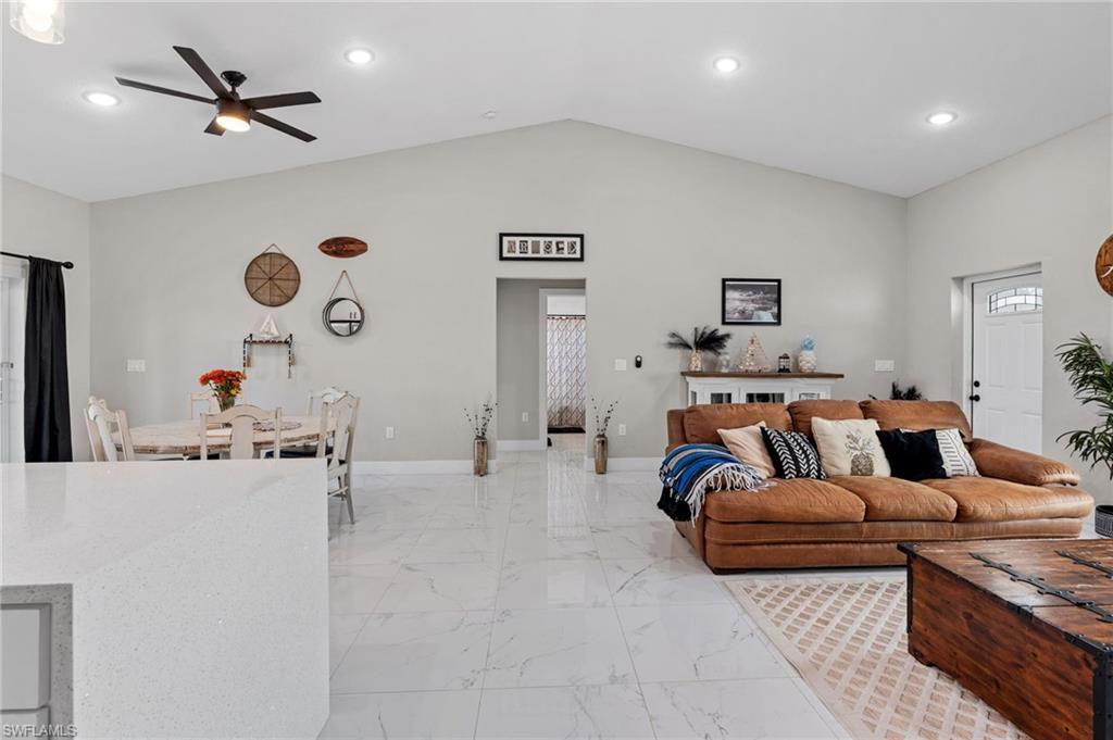 Living room featuring vaulted ceiling, recessed lighting, light marble finish floors, and a ceiling fan