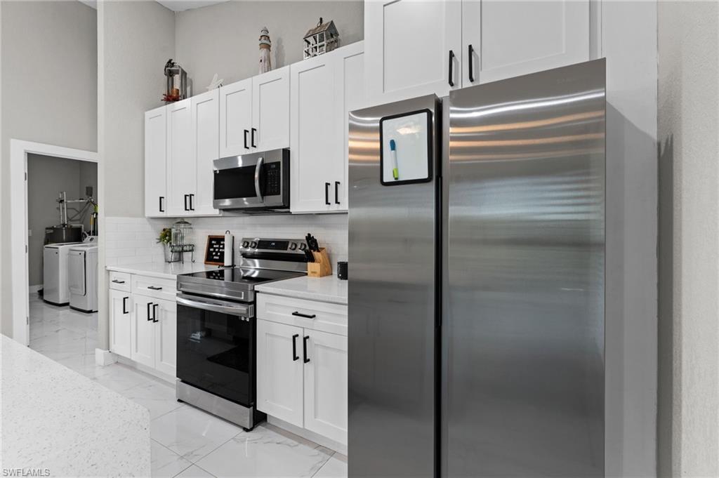 Kitchen with stainless steel appliances, separate washer and dryer, light stone counters, light marble finish flooring, and white cabinets