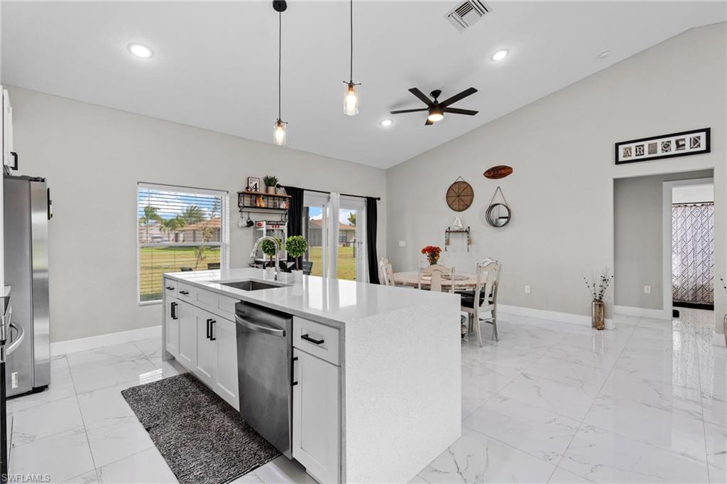 Kitchen featuring white cabinetry, lofted ceiling, pendant lighting, light stone counters, and stainless steel appliances