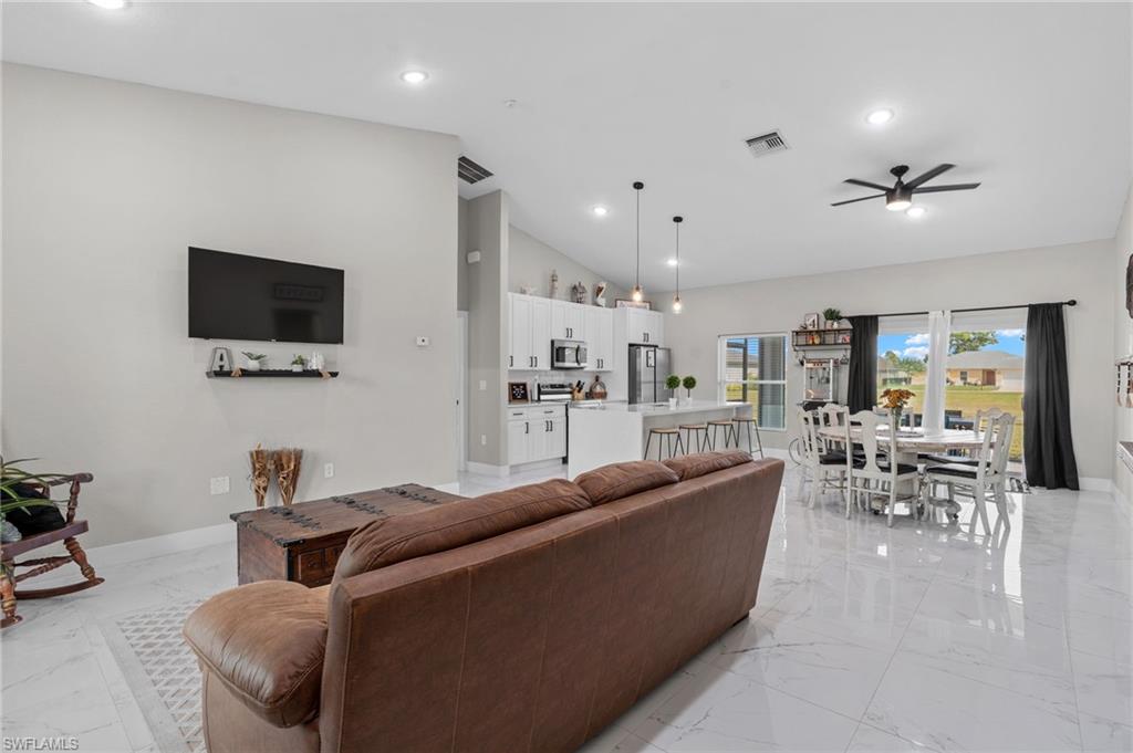 Living room with vaulted ceiling, a ceiling fan, recessed lighting, and light marble finish flooring