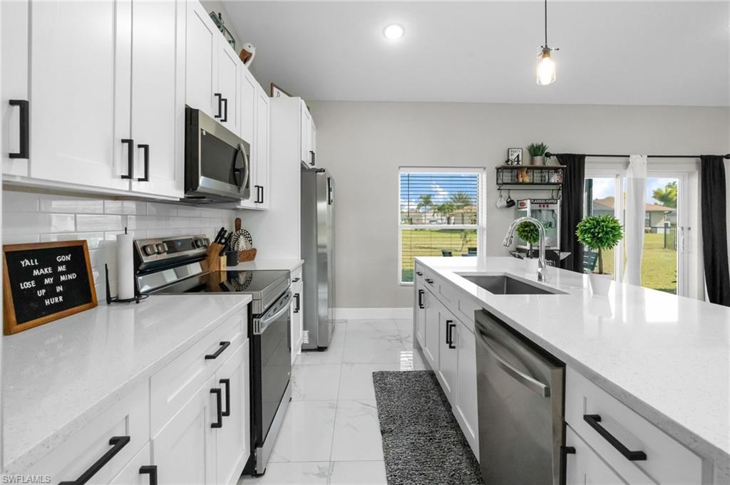 Kitchen featuring appliances with stainless steel finishes, white cabinets, light stone counters, hanging light fixtures, and recessed lighting