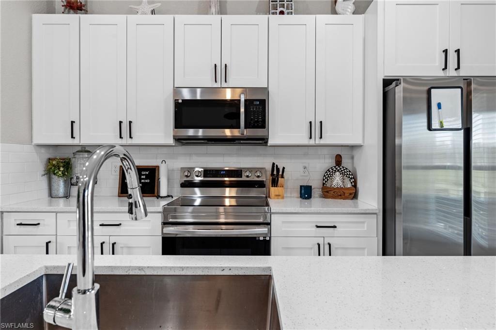 Kitchen featuring appliances with stainless steel finishes, backsplash, and white cabinetry