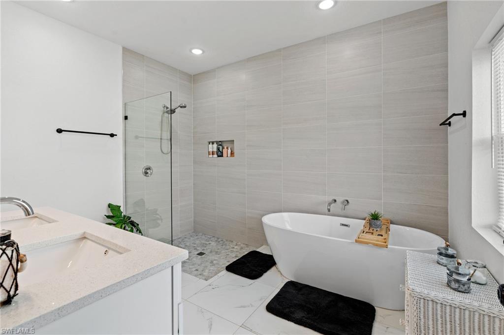 Bathroom featuring a freestanding tub, double vanity, walk in shower, light marble finish flooring, and recessed lighting