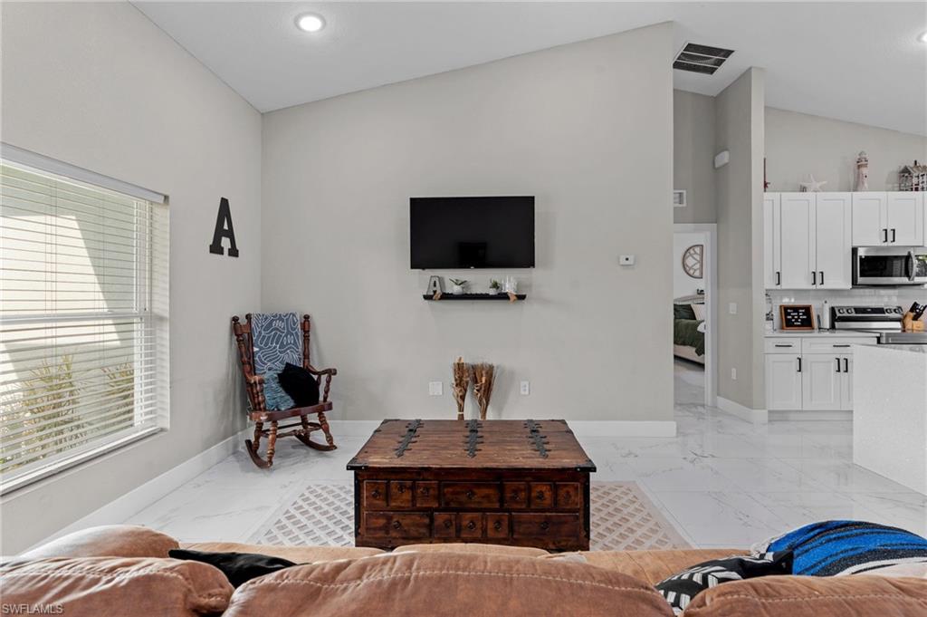 Living area featuring vaulted ceiling, recessed lighting, and light marble finish flooring