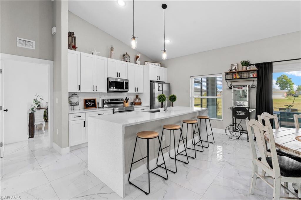 Kitchen with pendant lighting, appliances with stainless steel finishes, white cabinetry, light stone counters, and a breakfast bar area