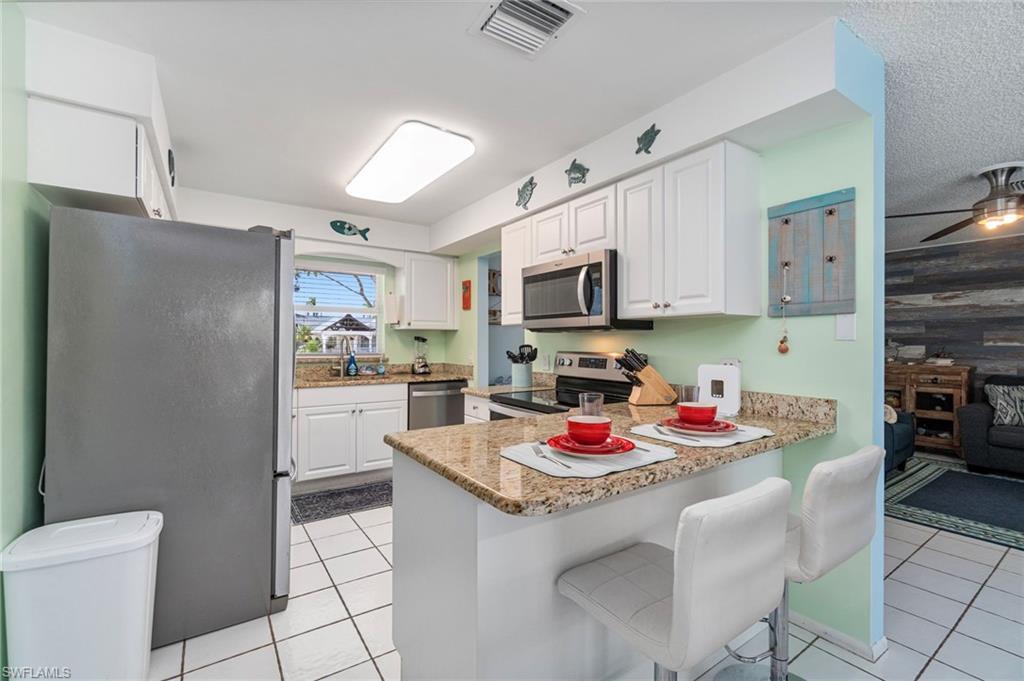 Kitchen with stainless steel appliances, white cabinetry, a peninsula, and light tile patterned floors