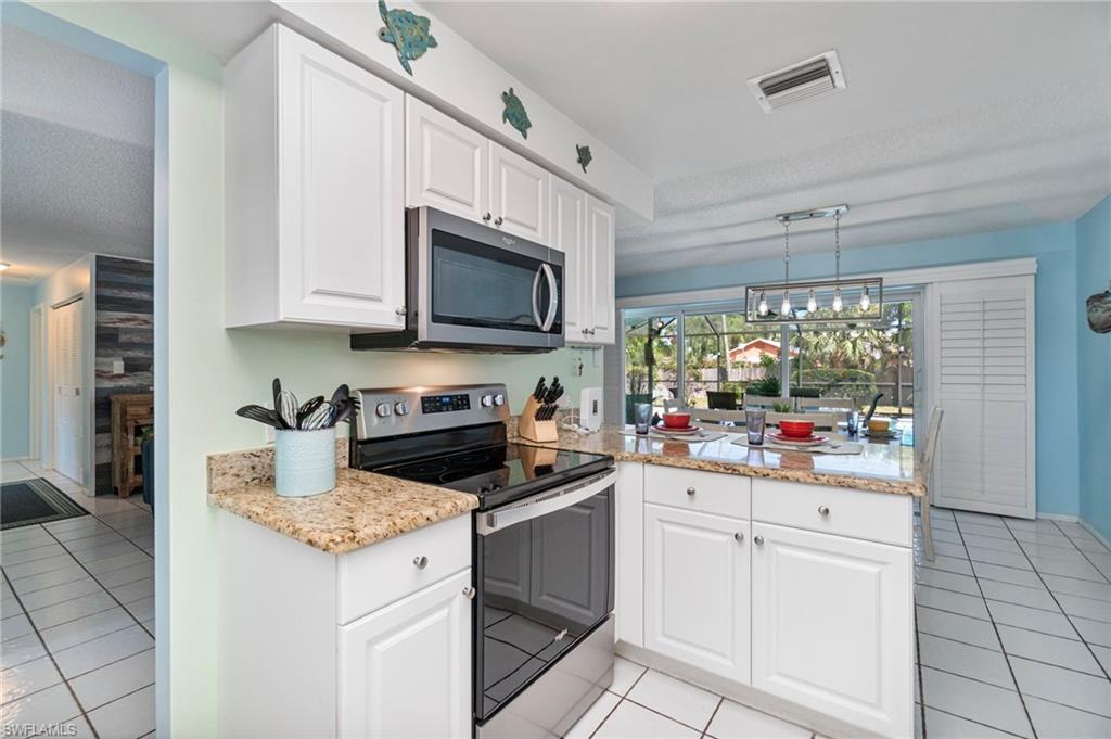 Kitchen featuring stainless steel appliances, light tile patterned floors, white cabinets, light stone counters, and a textured ceiling