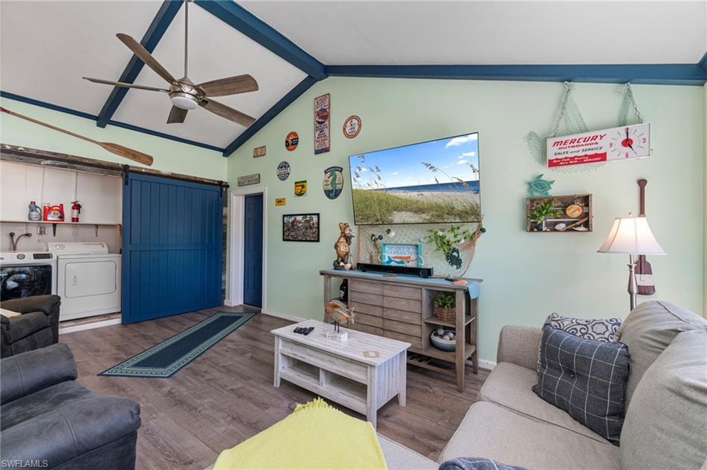 Living area with a barn door, beamed ceiling, wood finished floors, ceiling fan, and washing machine and dryer