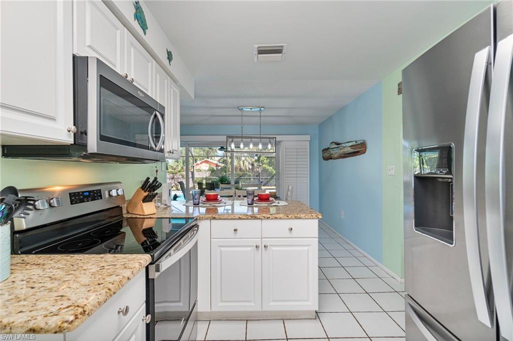 Kitchen featuring stainless steel appliances, white cabinetry, light tile patterned flooring, light stone counters, and a peninsula