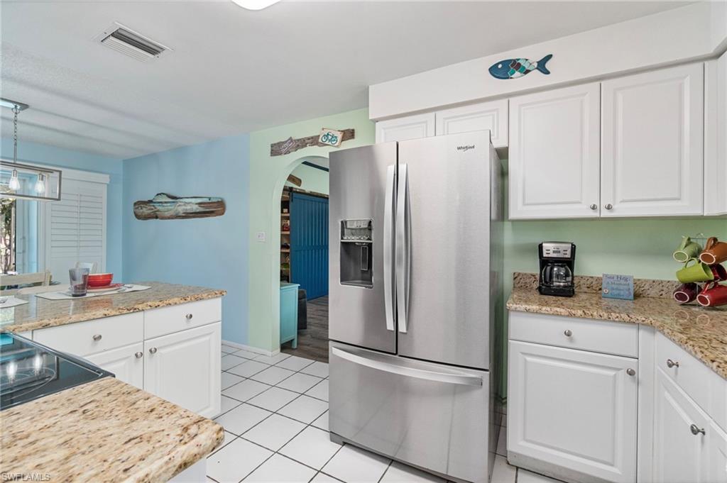 Kitchen featuring stainless steel refrigerator with ice dispenser, white cabinets, light stone counters, light tile patterned floors, and pendant lighting