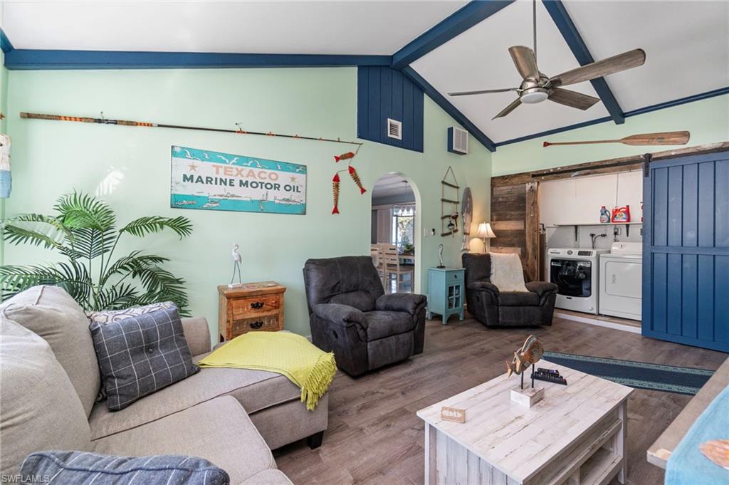 Living area with arched walkways, wood finished floors, beam ceiling, a ceiling fan, and washer and clothes dryer