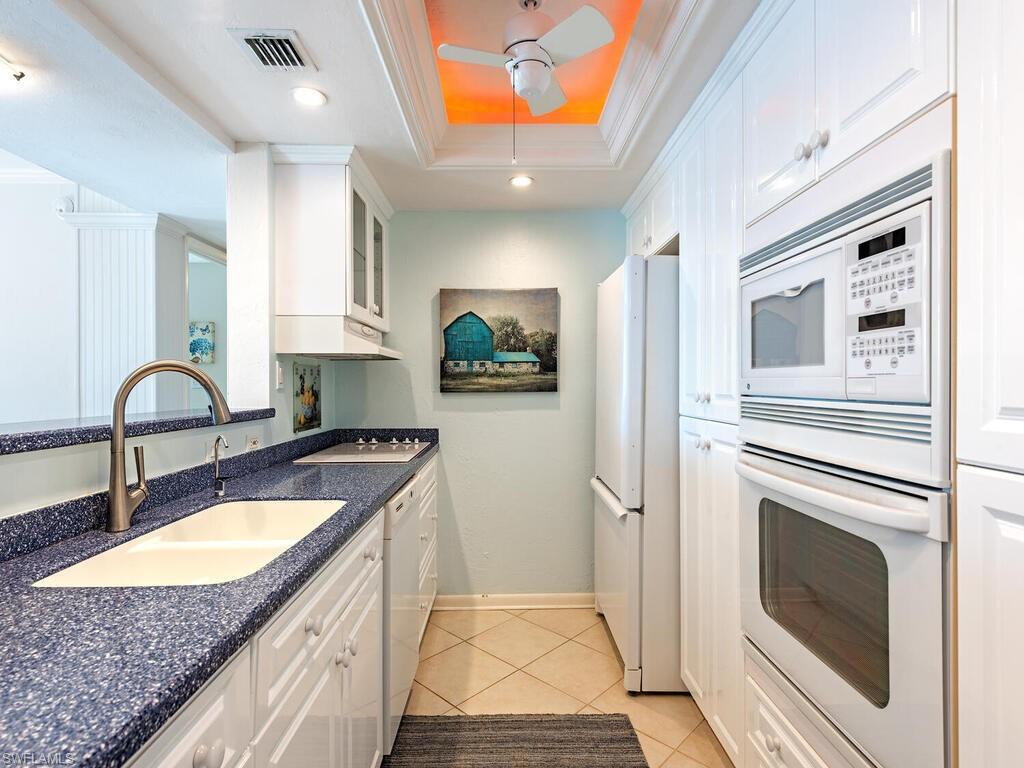Kitchen with white cabinetry, white appliances, light tile patterned floors, crown molding, and glass insert cabinets