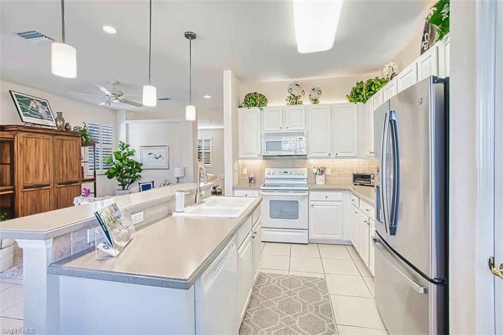 Kitchen with white appliances, decorative backsplash, decorative light fixtures, white cabinetry, and light tile patterned flooring