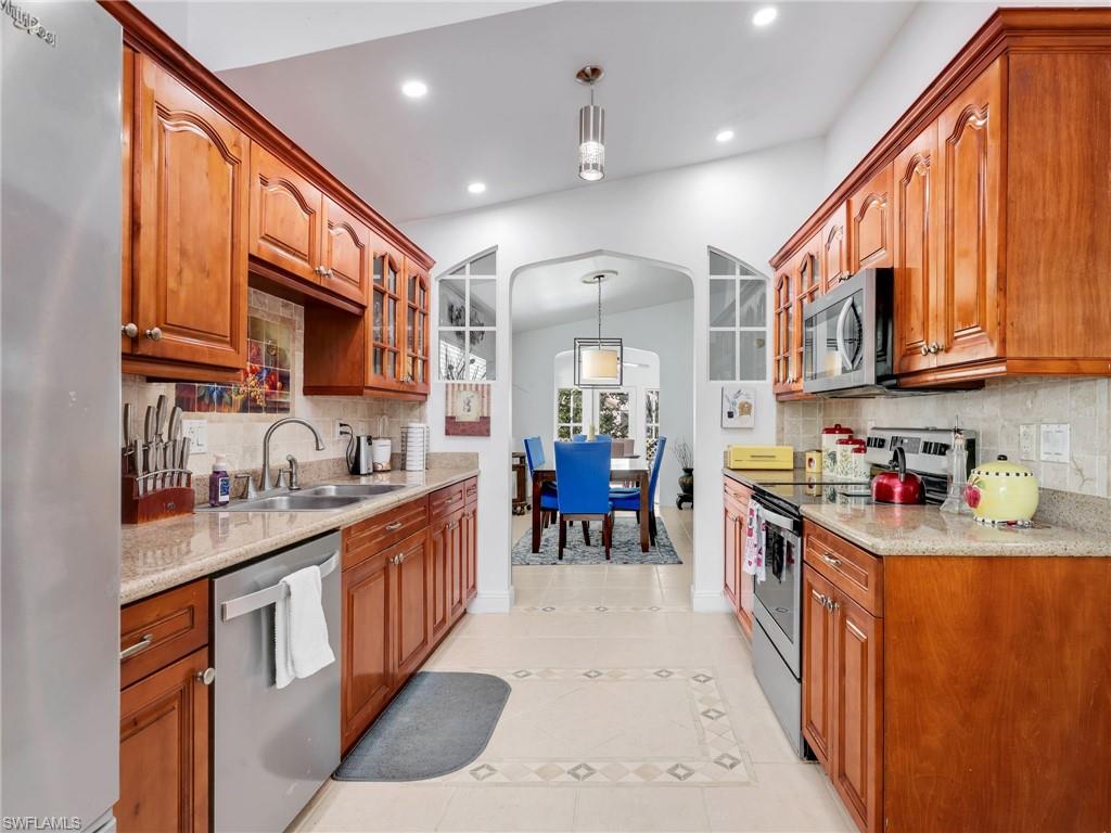Kitchen featuring decorative light fixtures, arched walkways, appliances with stainless steel finishes, glass insert cabinets, and vaulted ceiling