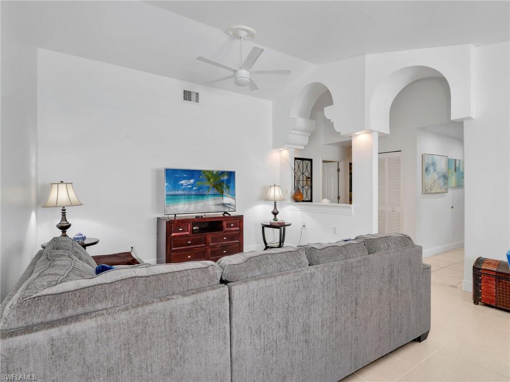 Living area featuring tile patterned flooring, a ceiling fan, arched walkways, and lofted ceiling