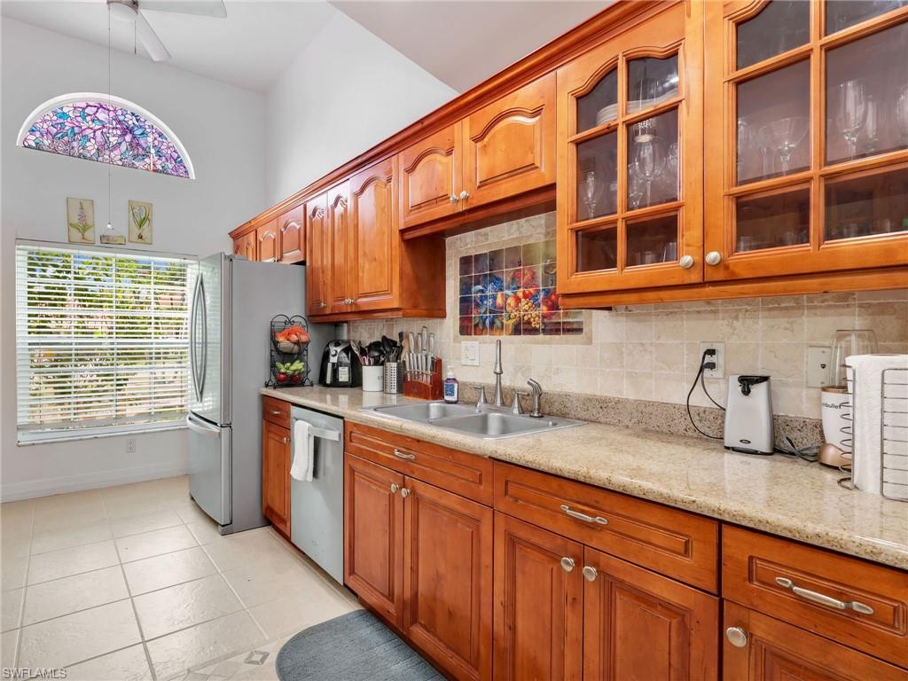 Kitchen featuring glass insert cabinets, tasteful backsplash, brown cabinetry, and stainless steel dishwasher