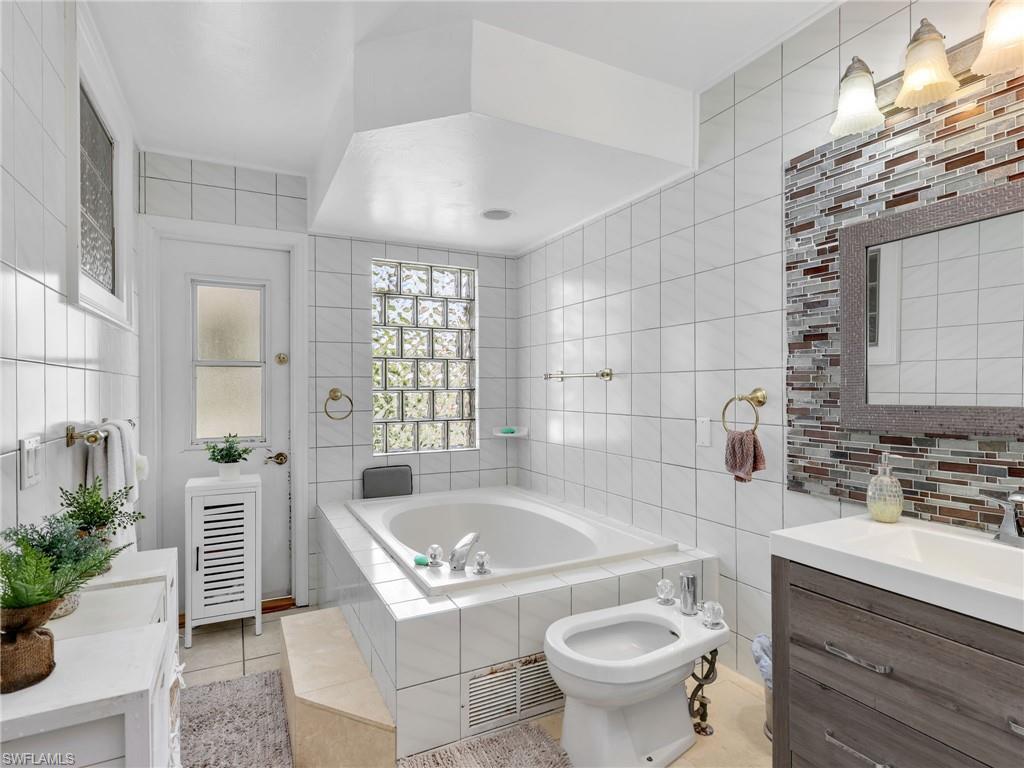 Bathroom featuring tile walls, vanity, a bath, a bidet, and light tile patterned floors