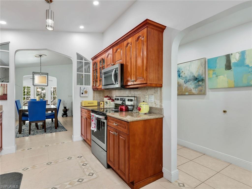 Kitchen with arched walkways, pendant lighting, appliances with stainless steel finishes, light tile patterned floors, and light stone countertops