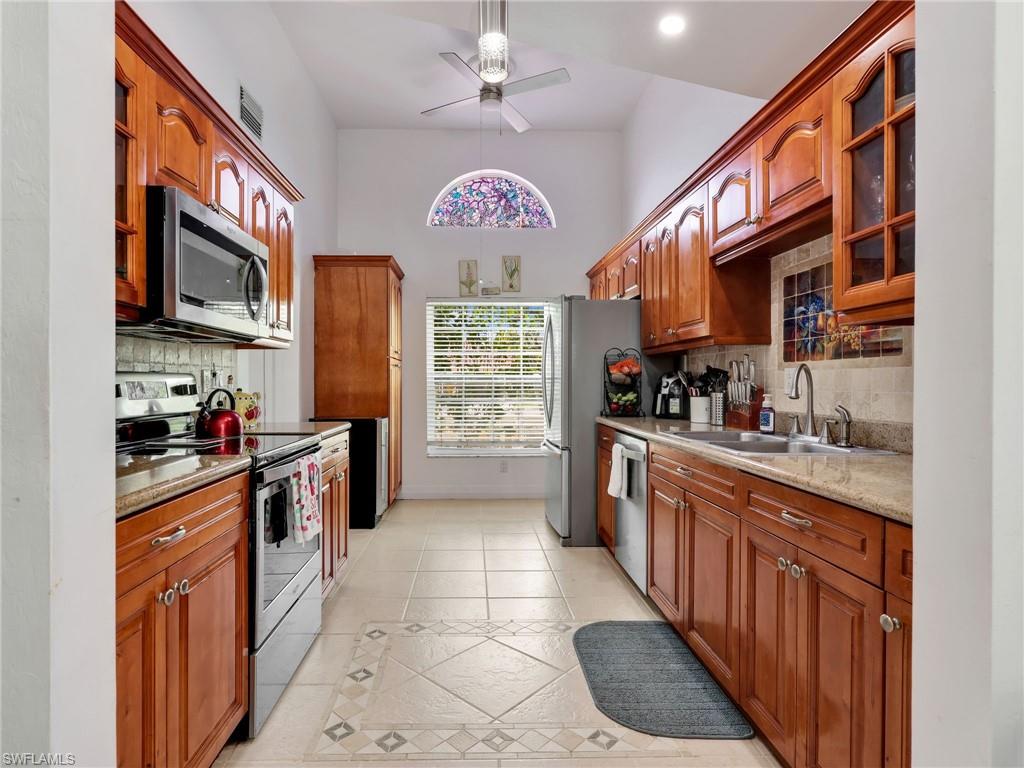 Kitchen featuring stainless steel appliances, light stone countertops, ceiling fan, and glass insert cabinets
