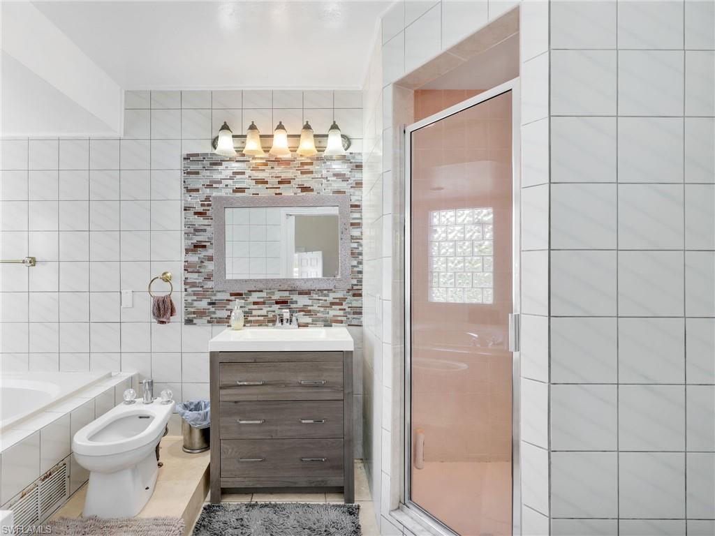Full bath featuring vanity, a bidet, tile walls, a shower stall, and a bath
