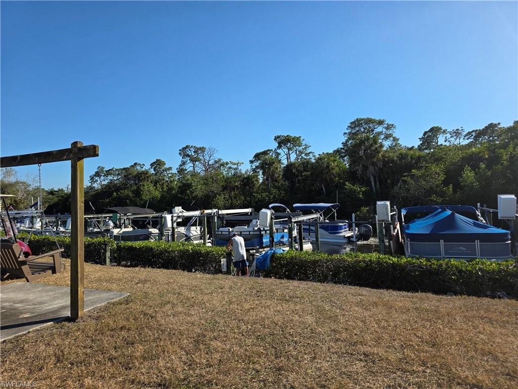 View of grassy yard with view of wooded area and a dock