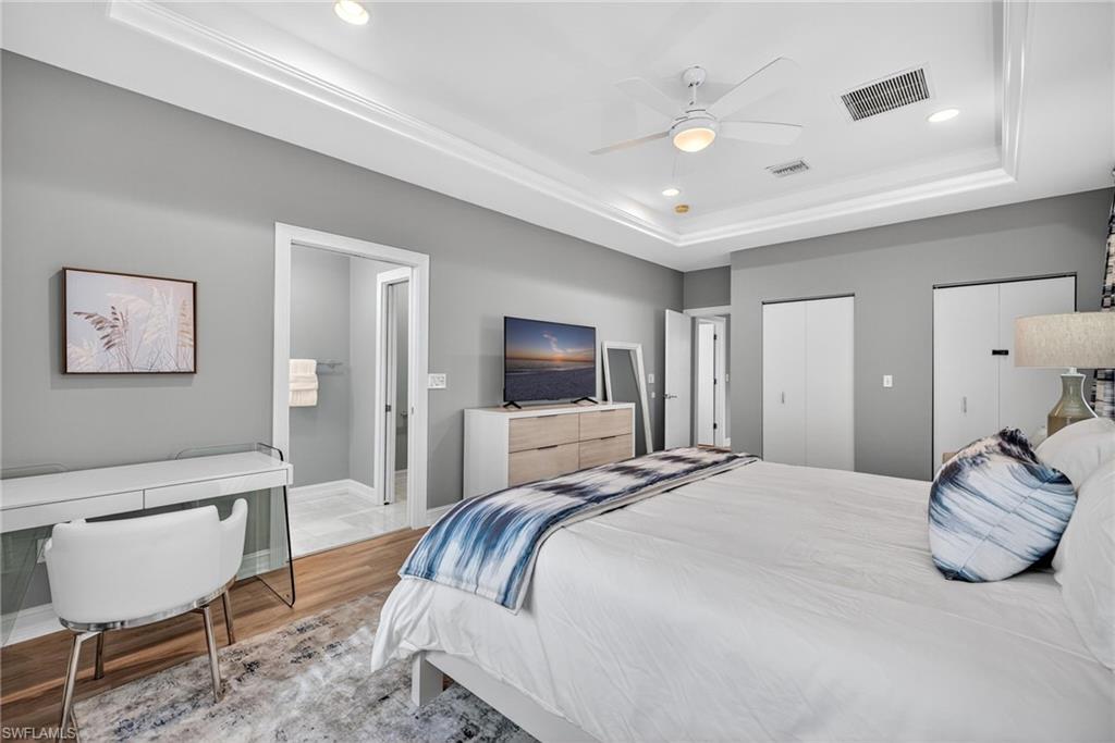 Bedroom featuring multiple closets, a raised ceiling, wood finished floors, recessed lighting, and ceiling fan