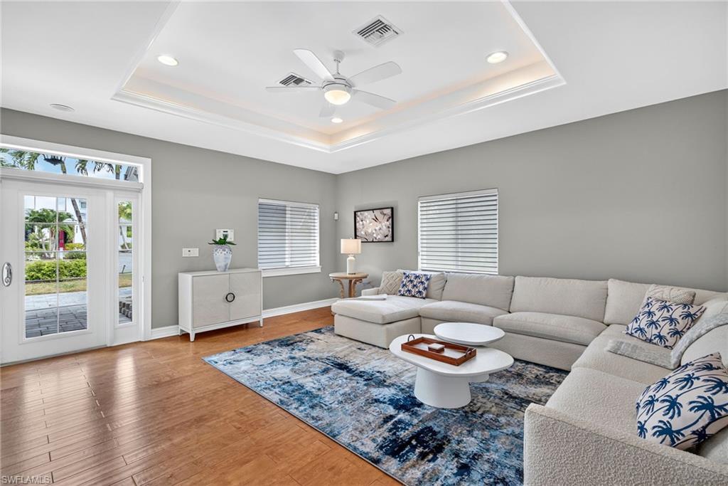 Living area with healthy amount of natural light, wood finished floors, a ceiling fan, a tray ceiling, and recessed lighting