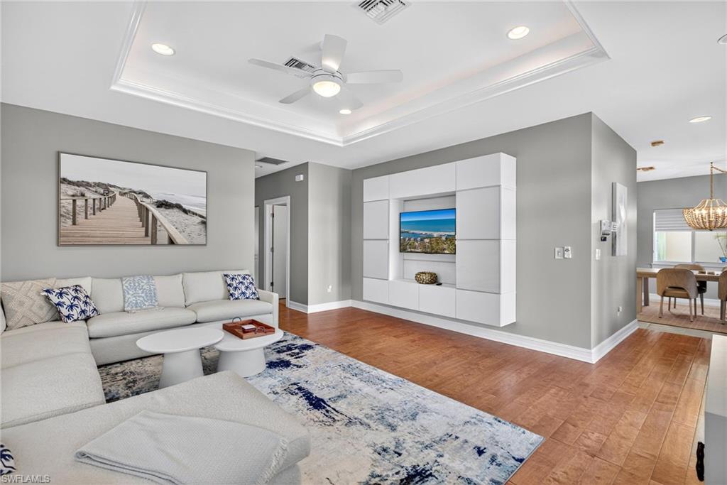 Living room featuring a raised ceiling, light wood finished floors, ceiling fan, and recessed lighting