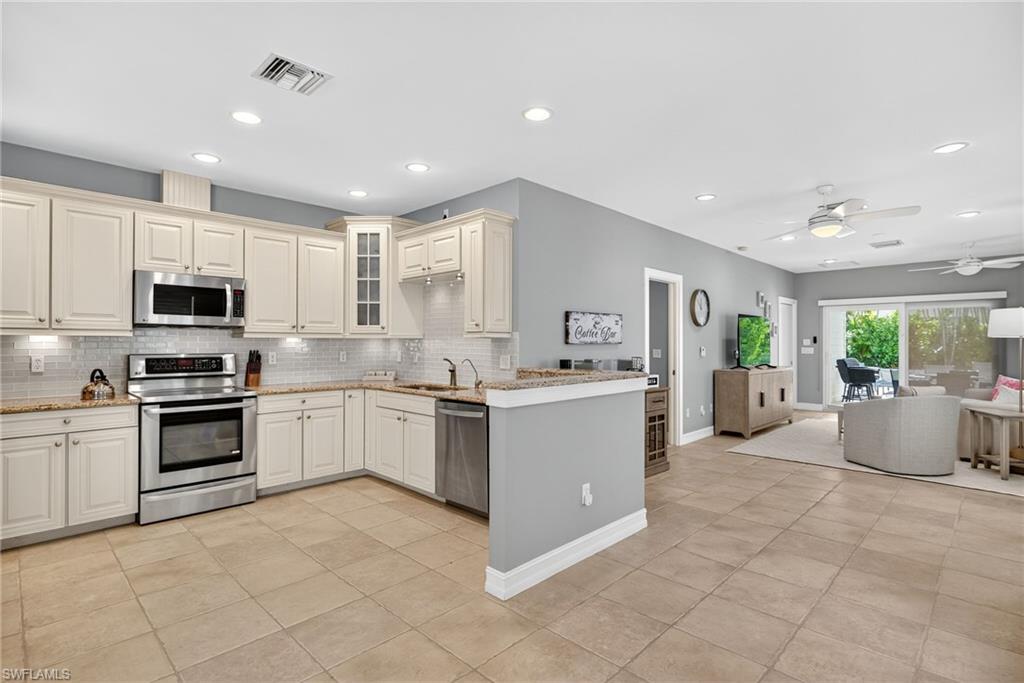 Kitchen featuring appliances with stainless steel finishes, ceiling fan, glass insert cabinets, light tile patterned flooring, and light stone countertops
