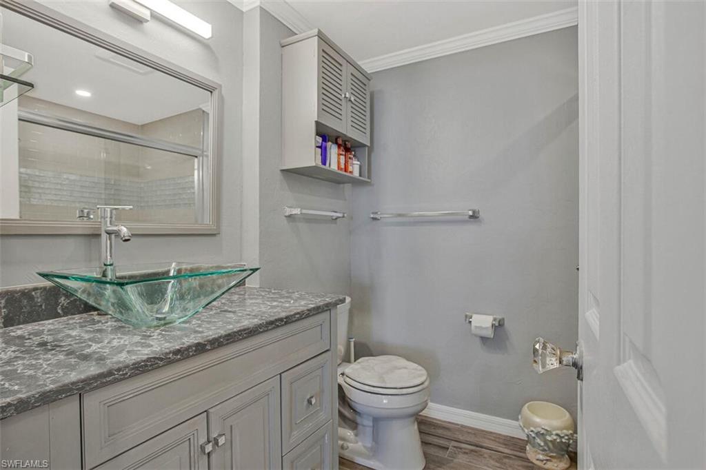Full bathroom featuring vanity, tiled shower, dark wood-style floors, and ornamental molding