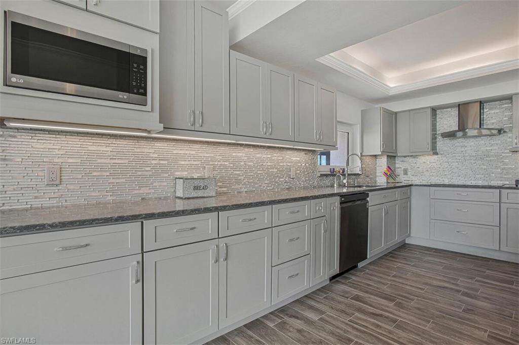 Kitchen with dark stone countertops, stainless steel microwave, wood finish floors, crown molding, and wall chimney exhaust hood