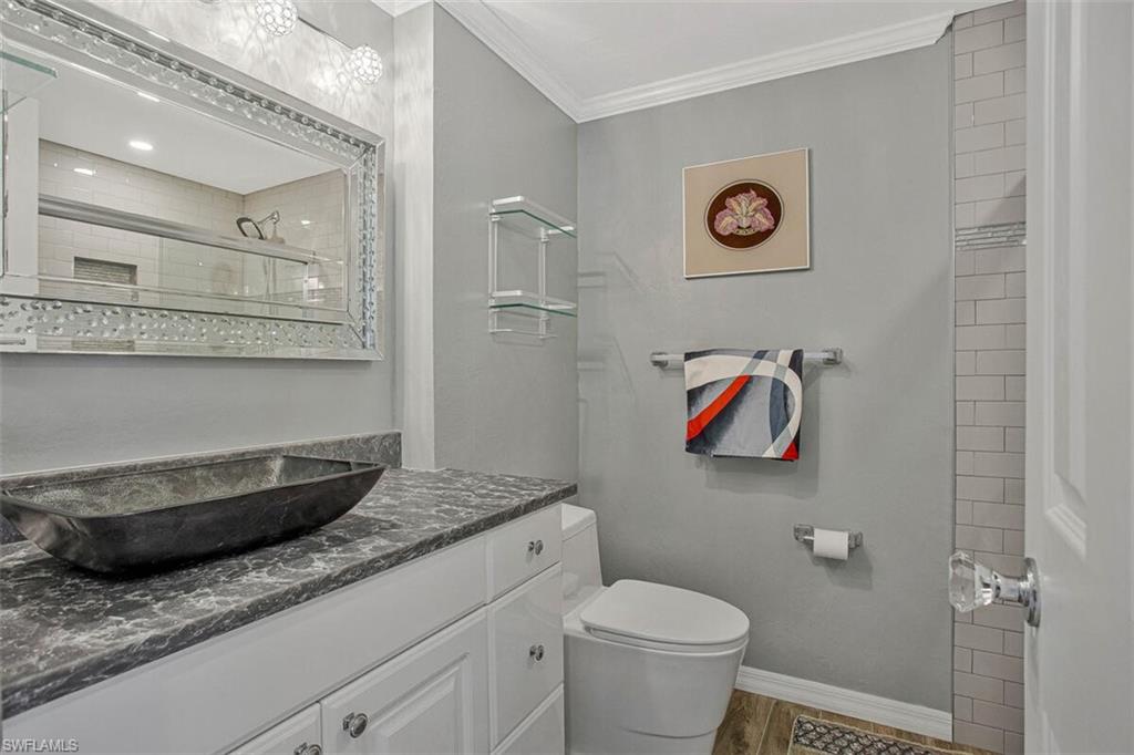 Bathroom with vanity, ornamental molding, a tile shower, and light wood-style flooring
