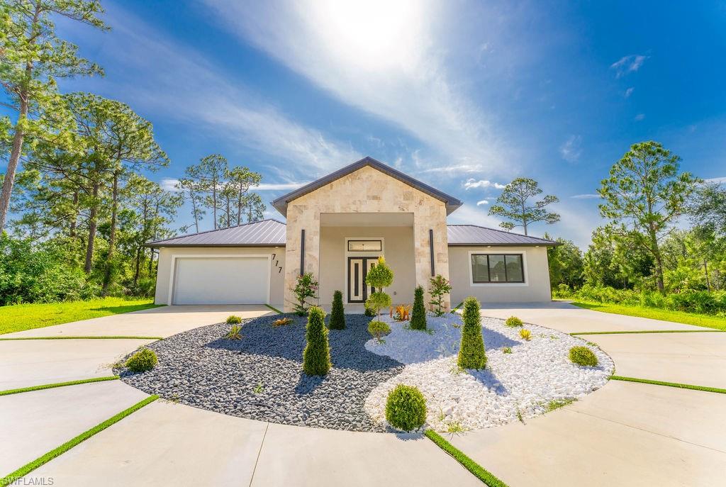View of front of property featuring a metal roof, concrete driveway, a standing seam roof, stucco siding, and an attached garage