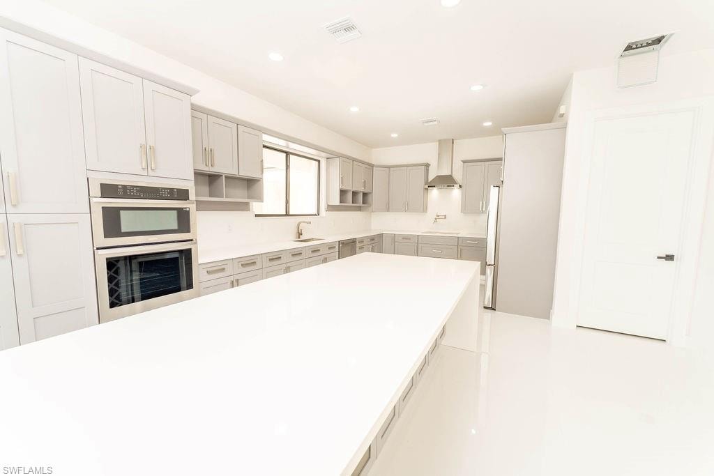Kitchen featuring recessed lighting, wall chimney range hood, stainless steel appliances, gray cabinetry, and open shelves