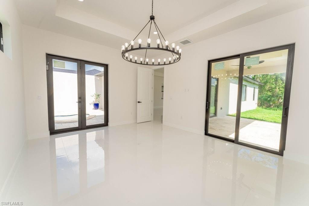 Unfurnished dining area with a raised ceiling, french doors, healthy amount of natural light, and a chandelier