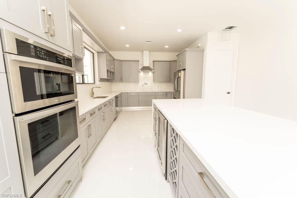 Kitchen with appliances with stainless steel finishes, gray cabinetry, recessed lighting, wall chimney exhaust hood, and light stone countertops