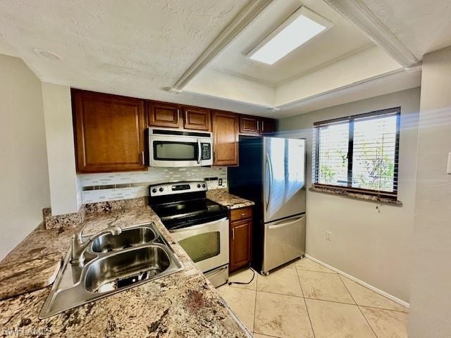 Kitchen with stainless steel appliances, backsplash, light tile patterned flooring, light stone countertops, and a tray ceiling