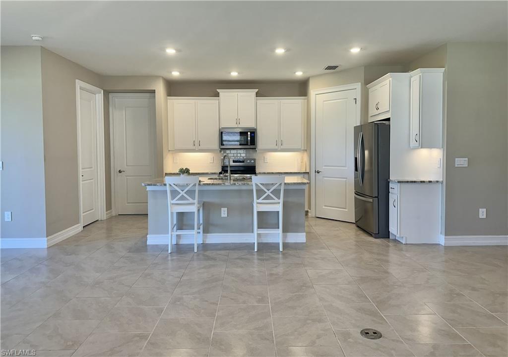 Kitchen with backsplash, white cabinets, stainless steel appliances, a kitchen island with sink, and a breakfast bar area