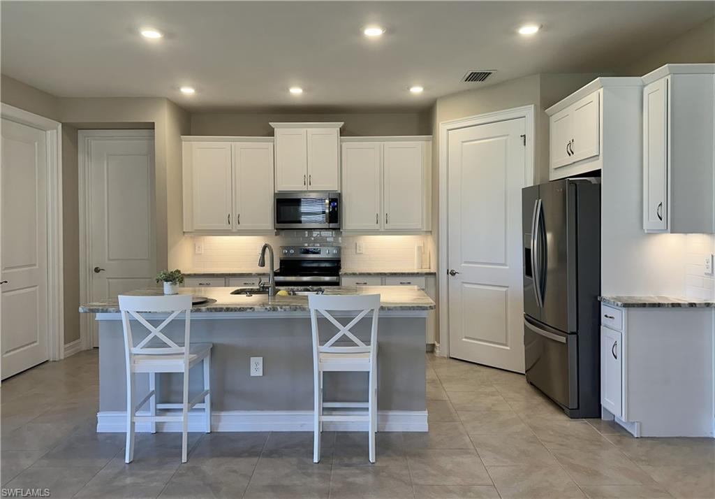 Kitchen featuring stainless steel appliances, backsplash, light stone counters, white cabinets, and an island with sink